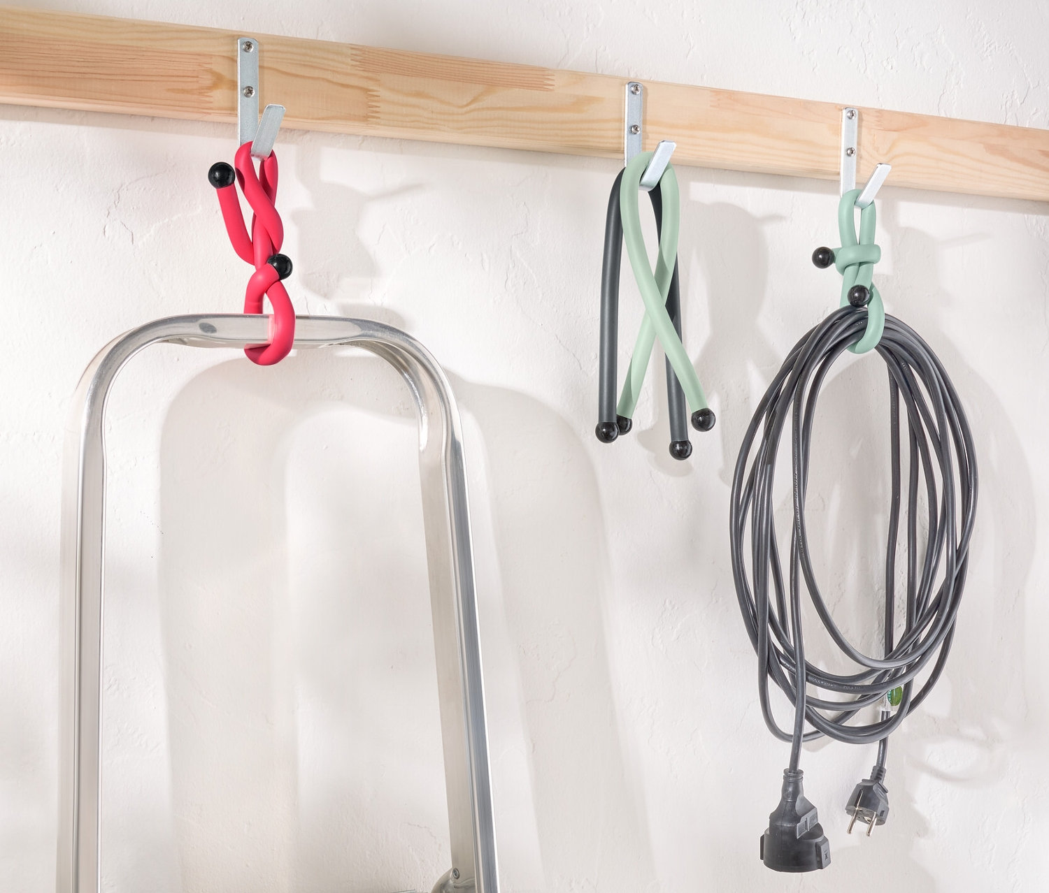 Une échelle est placée sous une latte en bois avec des crochets sur lesquels pendent des Power Kabelbinder en rouge, vert et noir.