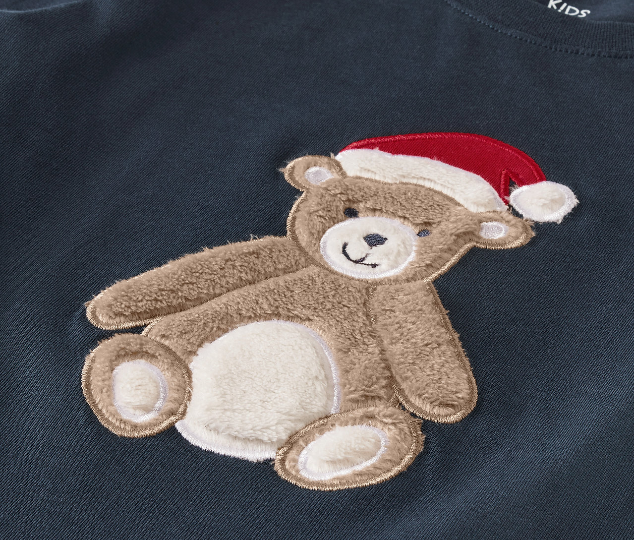 Broderie d'un ours en peluche avec un chapeau rouge sur un vêtement bleu foncé.