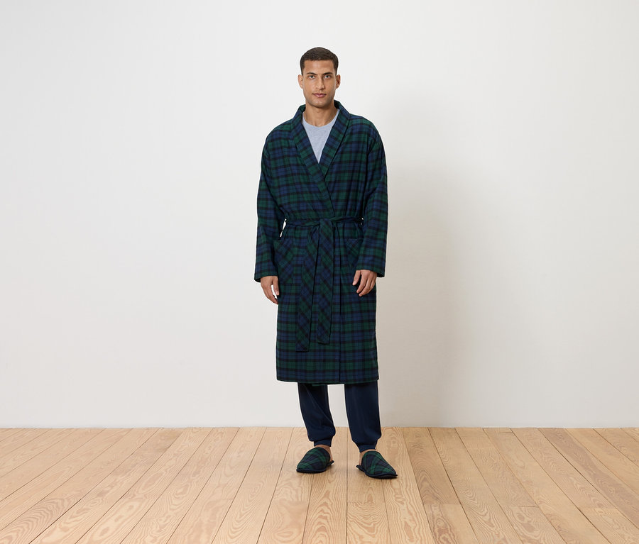 Un homme debout portant un peignoir à carreaux bleu et vert.