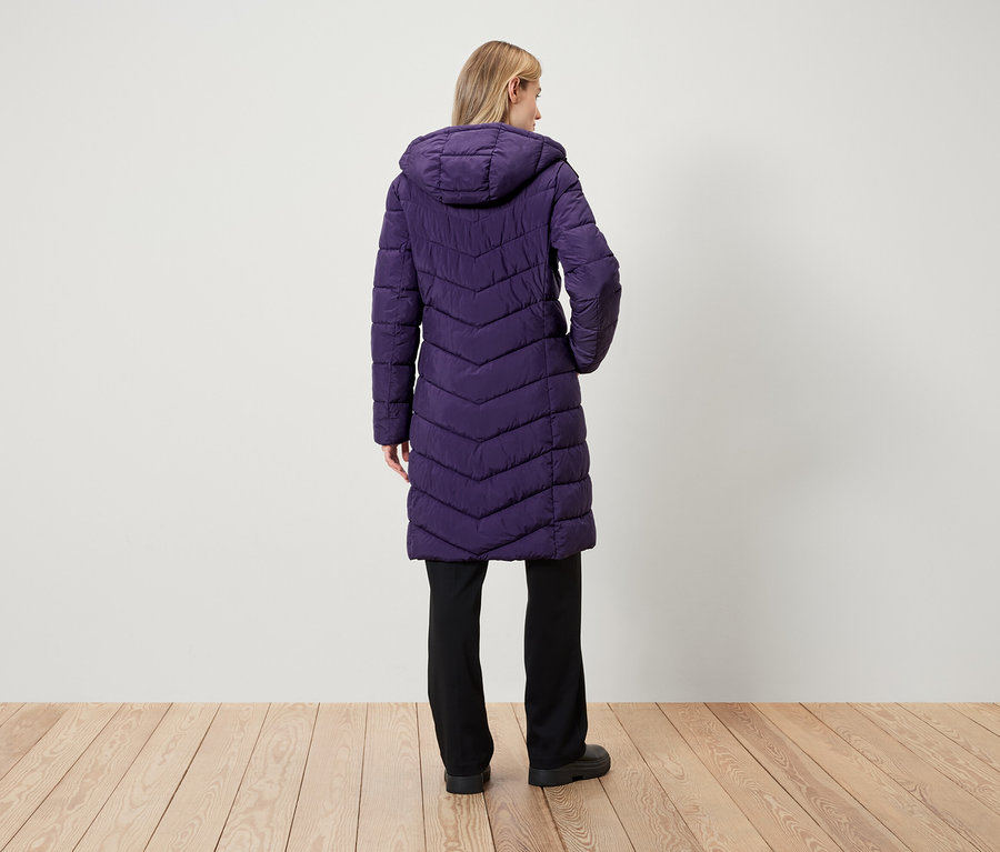 Une femme, vue de dos, porte un long manteau matelassé violet à capuche et un pantalon noir.