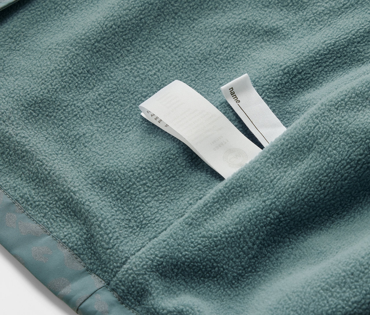 Détail d'une veste de pluie thermique pour enfant avec des éléments réfléchissants et une étiquette de nom.