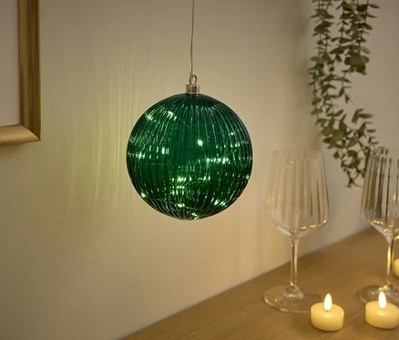 Une boule en verre verte avec des lumières suspendue au-dessus d'une table avec des verres et des bougies.