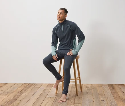 Un homme est assis sur un tabouret en bois et porte des sous-vêtements thermiques gris foncé.