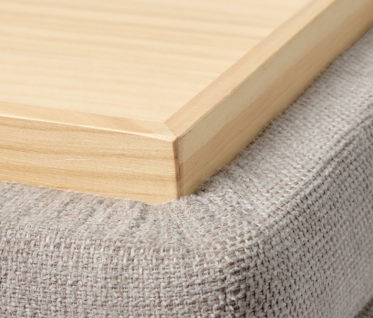 Gros plan d'un plateau en bois sur un pouf gris.