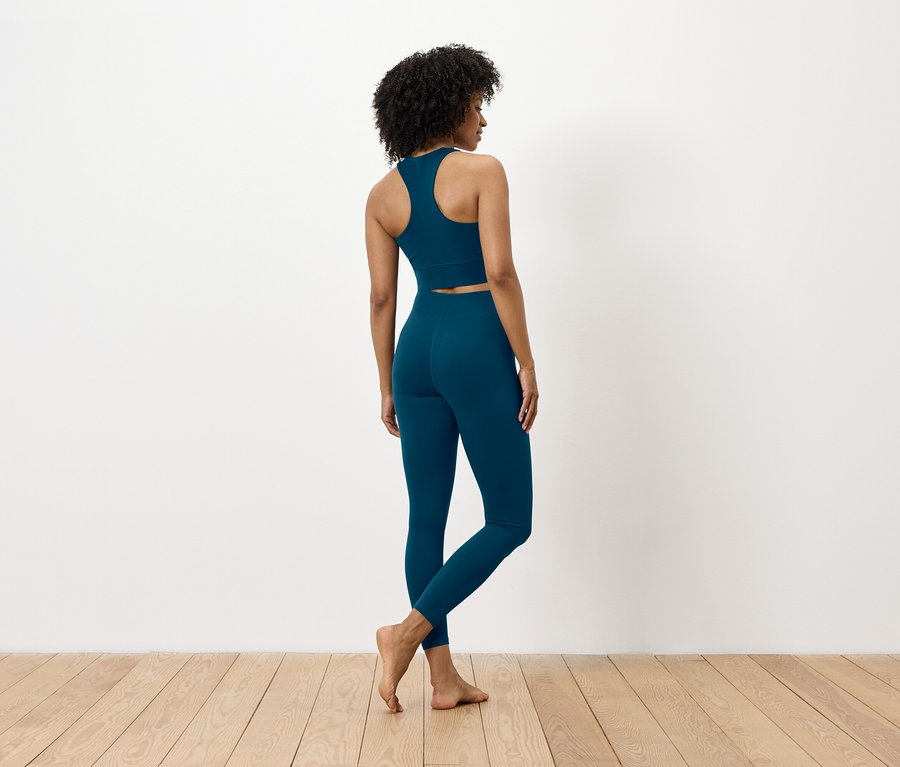 Vue de dos, une femme aux cheveux foncés portant un soutien-gorge de sport et un legging bleus.