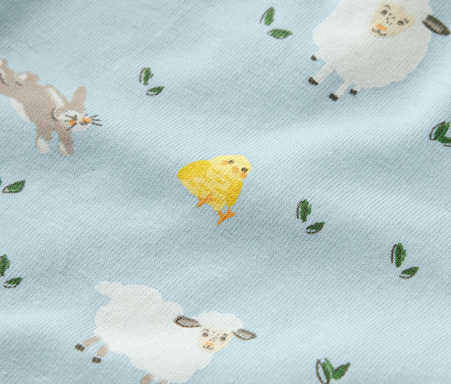 Gros plan sur un legging bleu pour enfant avec des motifs de moutons, de poussins, de lapins et de feuilles.
