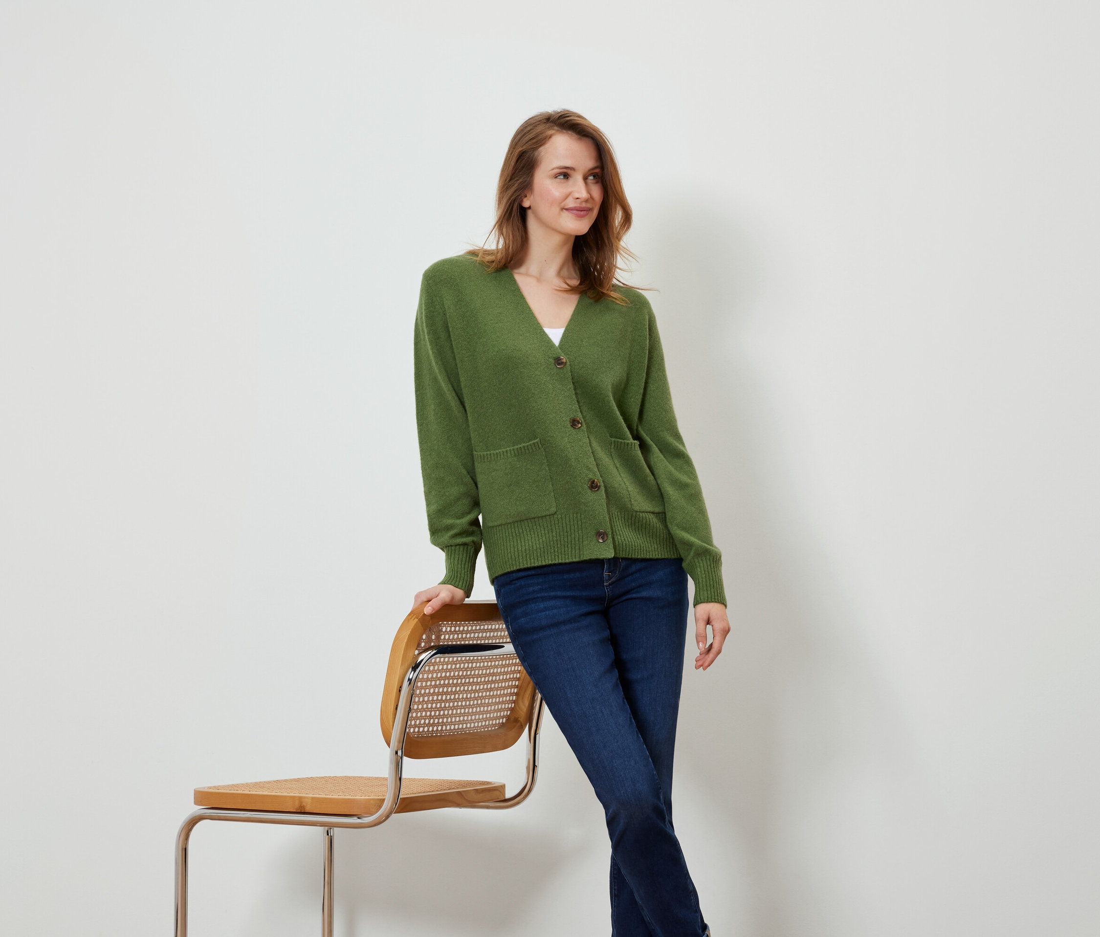 Femme en cardigan vert appuyée contre une chaise.