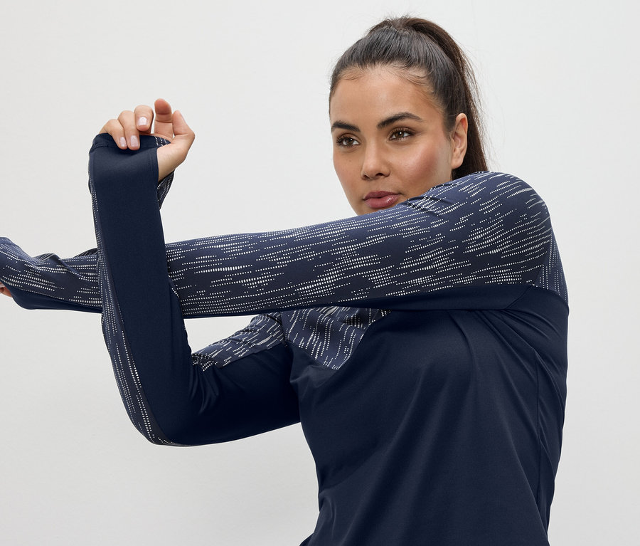 Femme étirant les bras dans un haut de sport bleu marine à manches longues avec des trous pour les pouces.