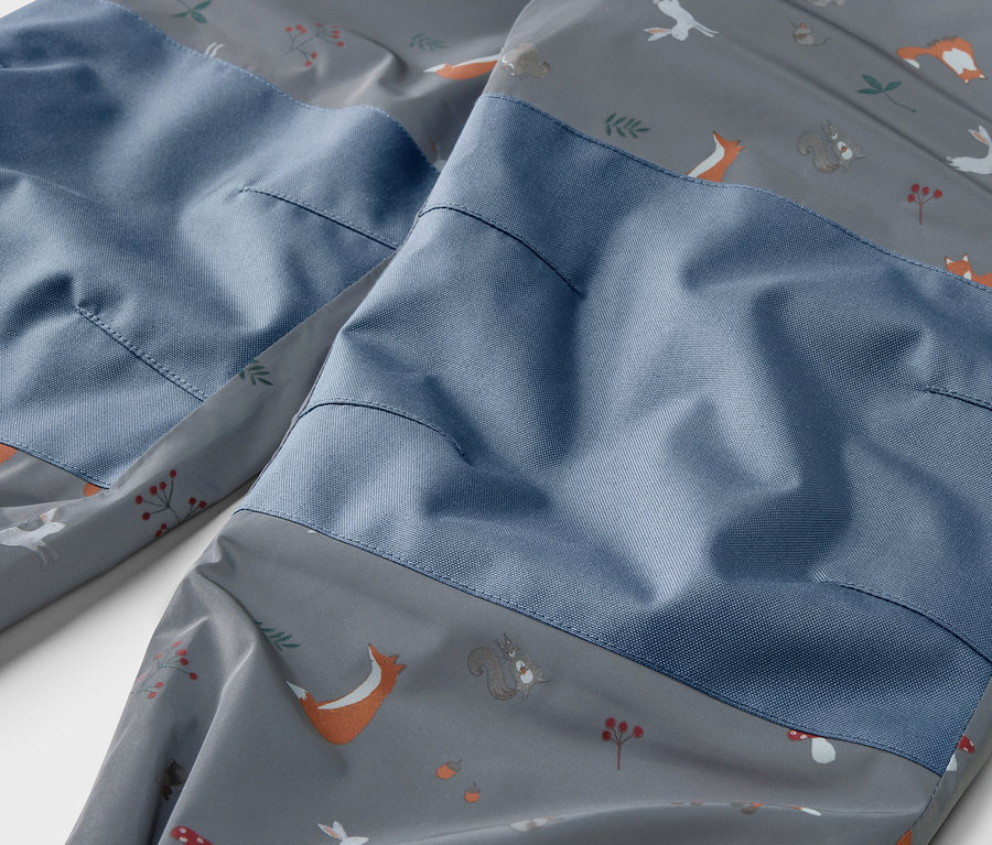 Gros plan sur un pantalon de pluie thermique pour enfants avec des éléments réfléchissants et un imprimé animalier.