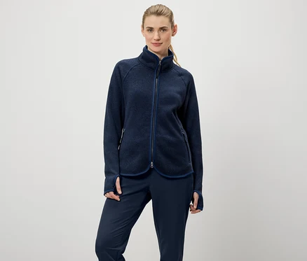 Une femme porte une veste polaire zippée bleu marine et un pantalon bleu marine.