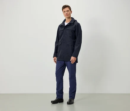 Un homme debout porte une veste bleu foncé à capuche, un pantalon bleu foncé et des chaussures noires.