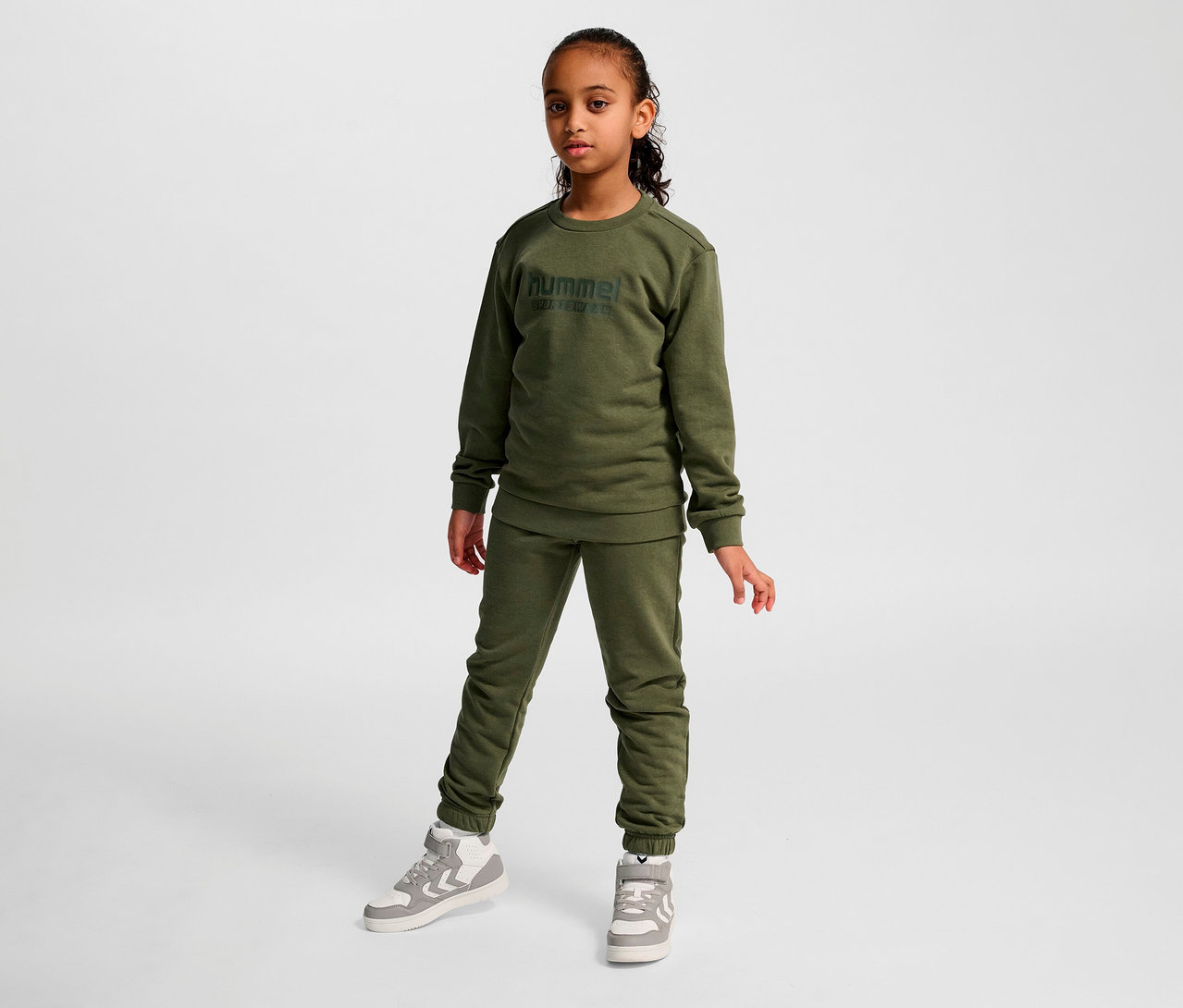 Une fille pose en survêtement et sweat-shirt HUMMEL HMLJR Base vert.