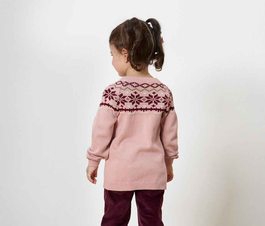 Fillette vue de dos, portant un pull rose avec un motif bordeaux et un pantalon bordeaux.