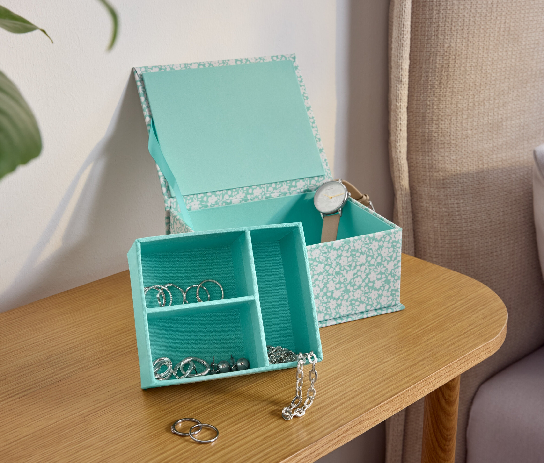 Une boîte à bijoux turquoise à motifs floraux sur une table de chevet en bois.