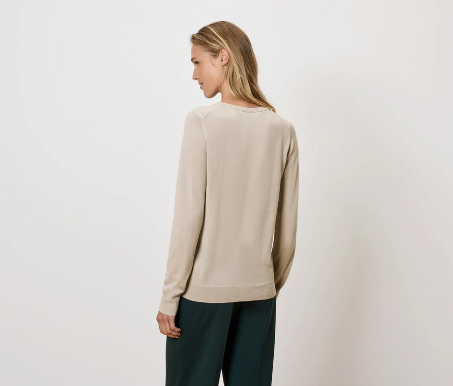 Une femme regarde par-dessus son épaule, portant un pull beige et un pantalon vert.