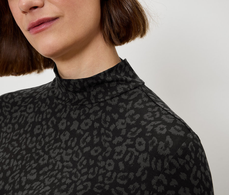 Gros plan sur le haut du corps d'une femme portant un col roulé à imprimé léopard noir et gris.