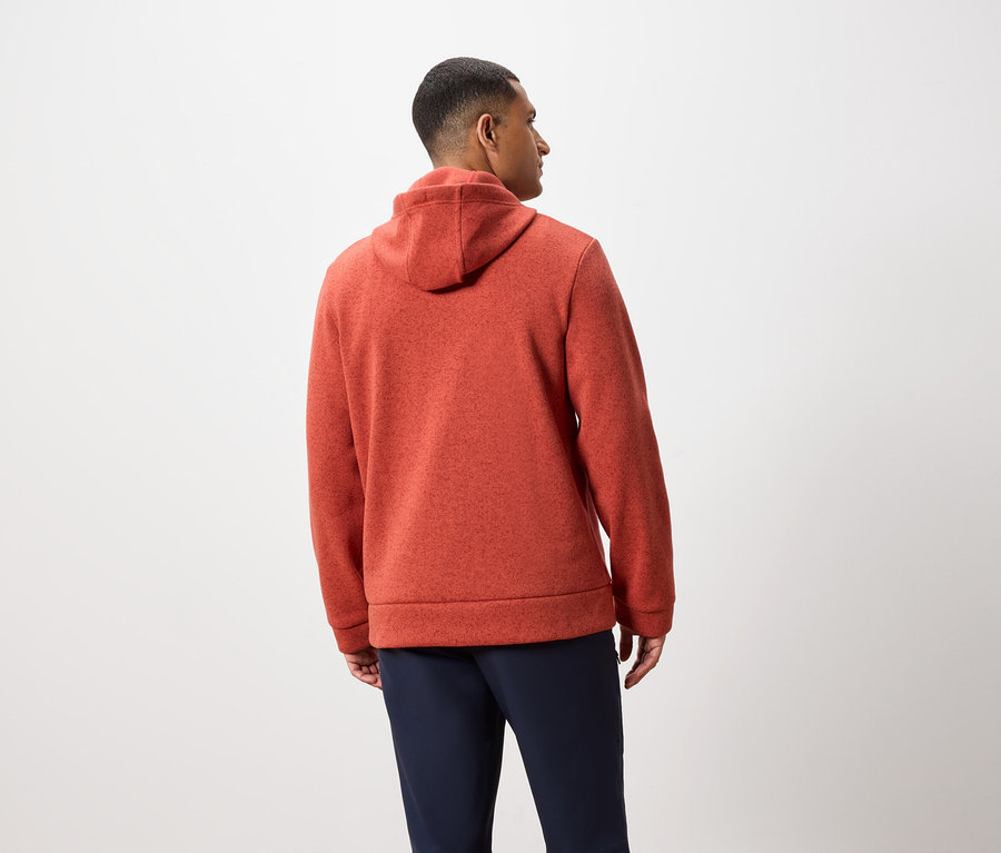 Un homme, vu de dos, porte un sweat à capuche orange et un pantalon bleu marine.