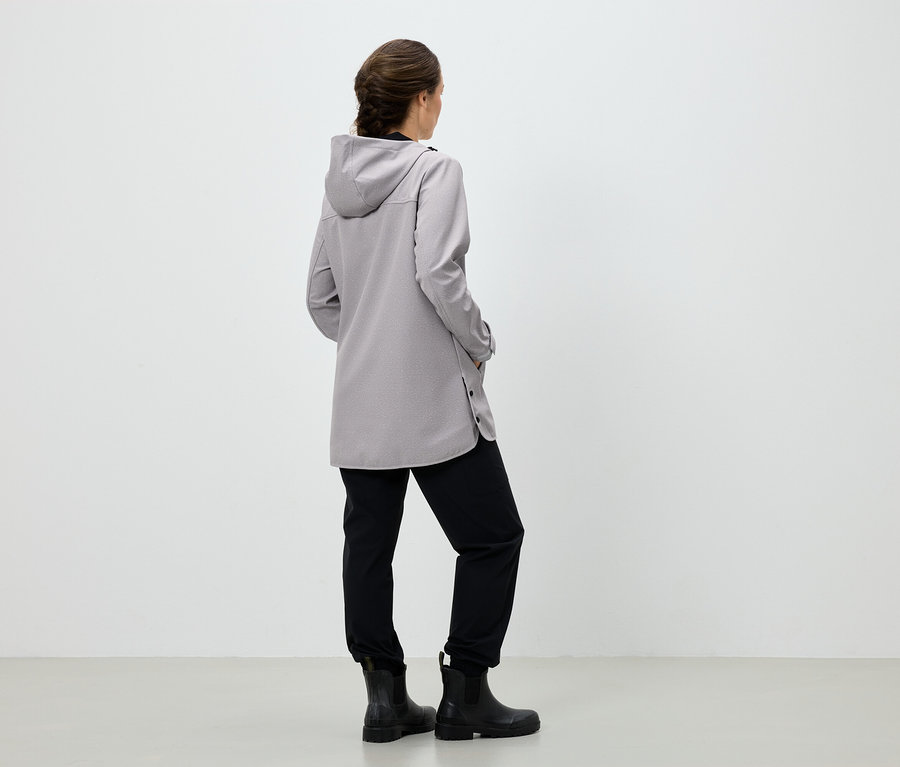 Une femme, dos à la caméra, porte un manteau gris à capuche, un pantalon noir et des bottes noires.