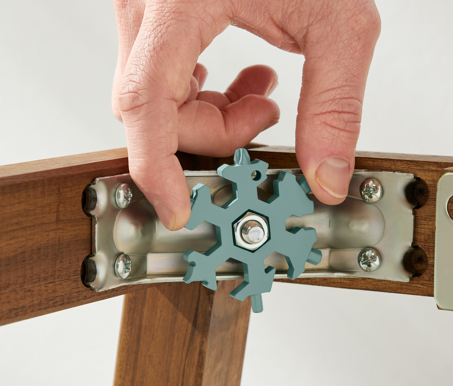 Une main tient une clé multifonctionnelle sur une vis sur un cadre en bois.