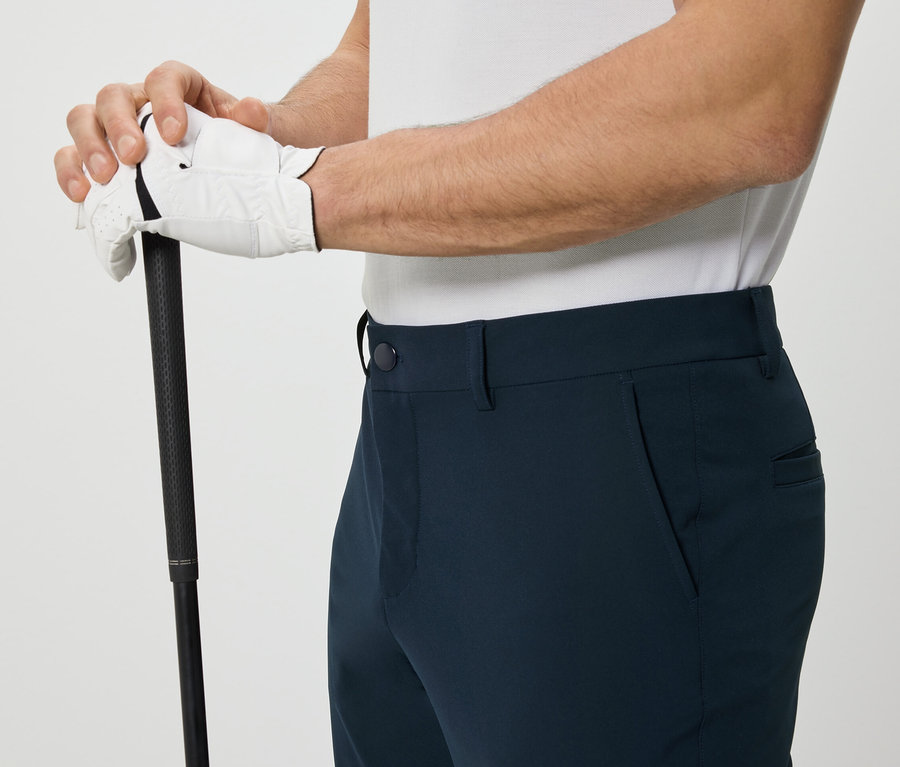 Homme tenant un club de golf et portant un pantalon d’extérieur.