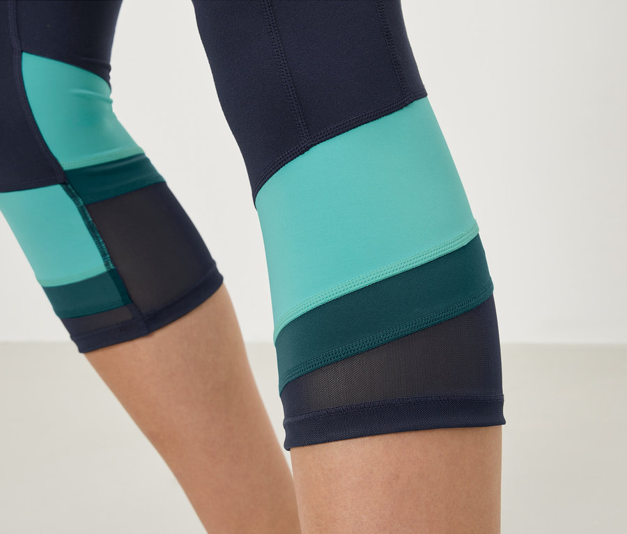 Gros plan sur un legging bleu marine avec des empiècements turquoise et vert foncé et des détails en maille.