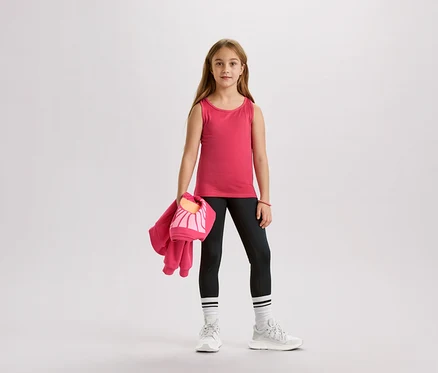 Fille portant un débardeur rose, un legging noir, des chaussettes blanches et des baskets, tenant une veste rose et un sac.