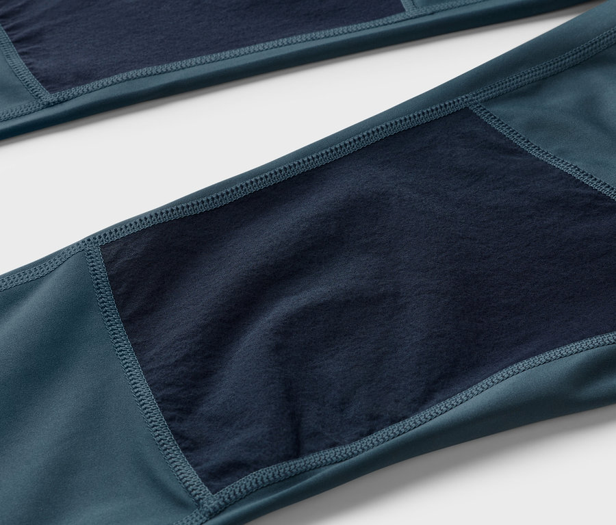 Gros plan d'un pantalon bleu-vert foncé avec des empiècements en tissu bleu marine aux genoux.