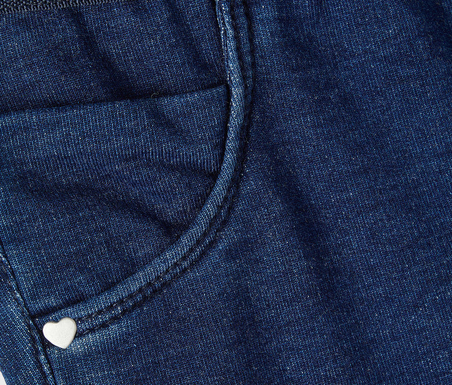 Gros plan sur un pantalon en jean bleu avec une petite poche et un bouton en forme de cœur.