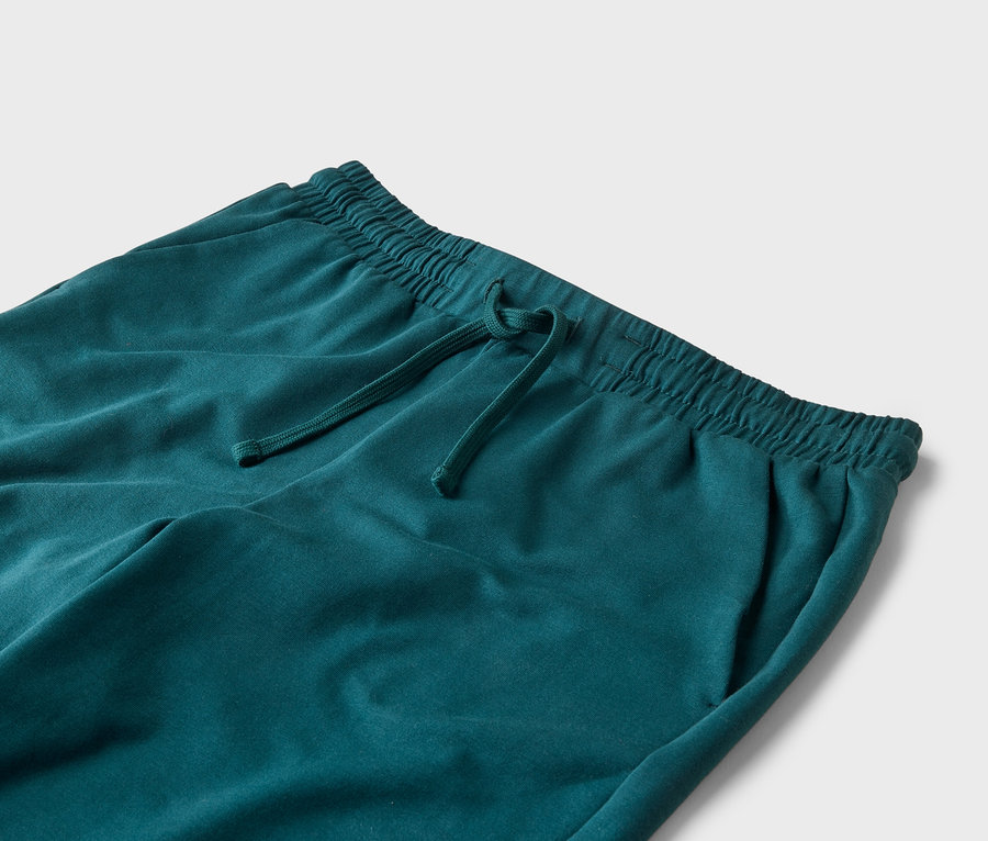 Gros plan d'un pantalon de survêtement turquoise avec cordon de serrage et taille élastique sur fond blanc.