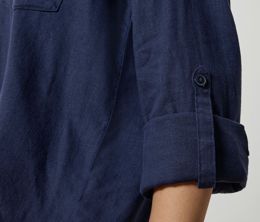 Gros plan sur une chemise en lin bleu marine avec des manches retroussées et des détails de boutons.