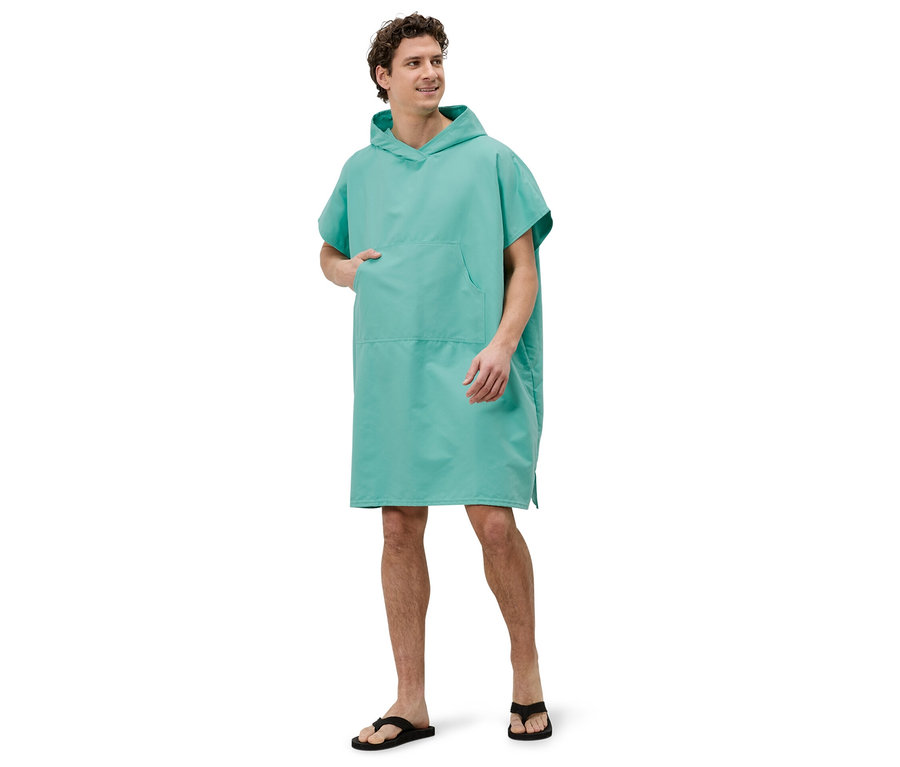 Un homme se tient sur un fond blanc, vêtu d'un poncho de bain turquoise à capuche et de tongs noires.
