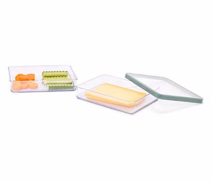 Deux récipients transparents contenant des morceaux de carottes et de concombres et des tranches de fromage, un couvercle vert est posé à côté.