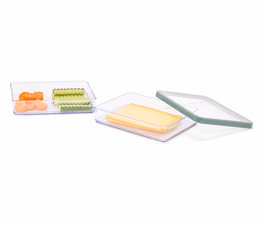 Deux récipients transparents contenant des morceaux de carottes et de concombres et des tranches de fromage, un couvercle vert est posé à côté.