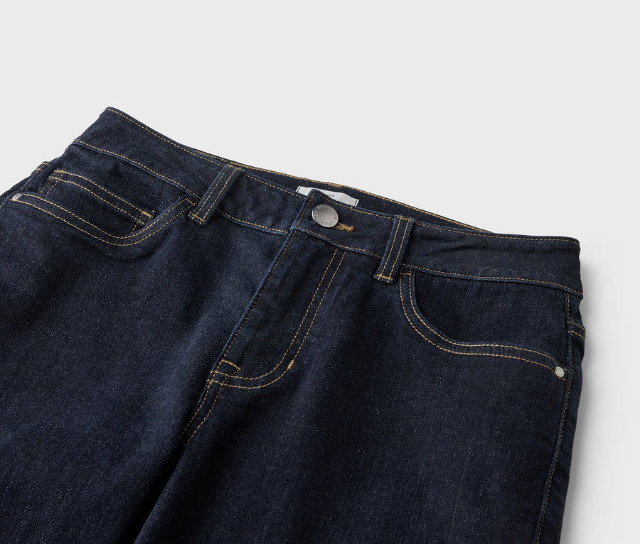 Gros plan d'un jean bleu foncé avec des coutures jaunes, un bouton et des poches sur un fond clair.