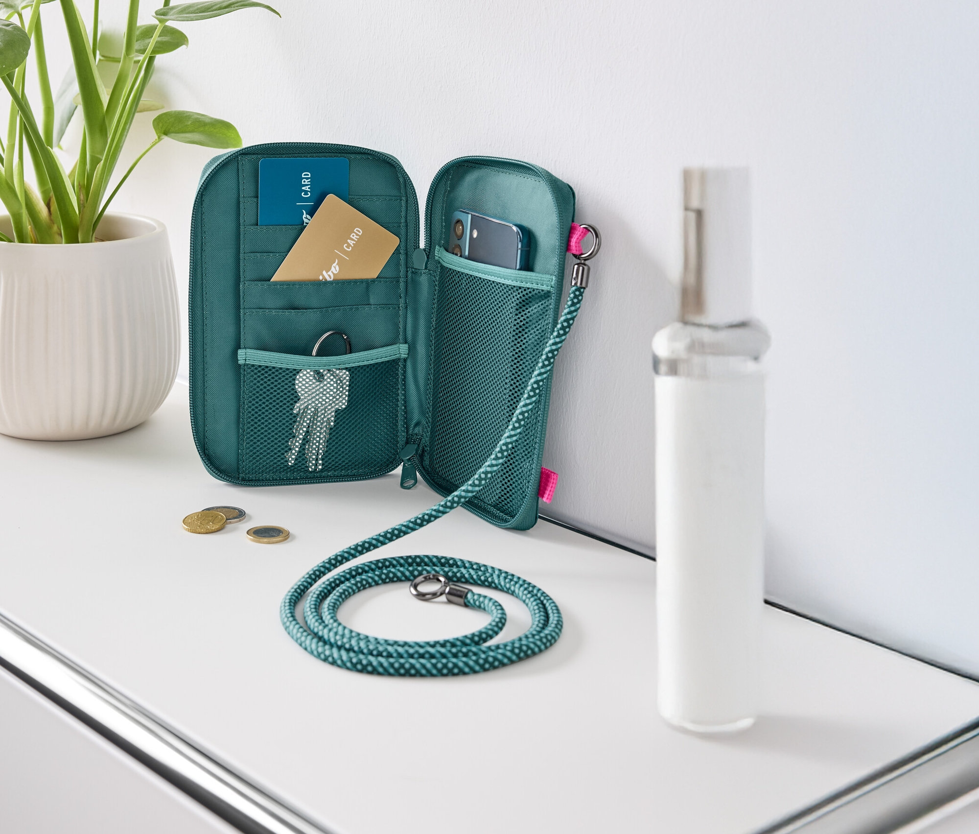 Un portefeuille vert ouvert posé sur une table blanche, rempli de cartes, de clés et d'un téléphone portable.