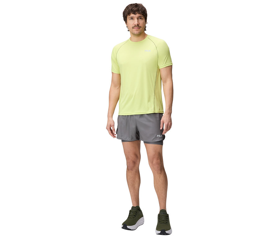Un homme debout portant un t-shirt jaune, un short gris et des chaussures vertes.
