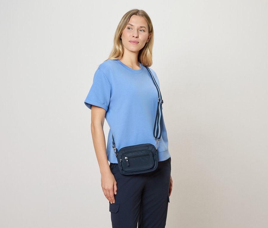 Femme portant un chemisier bleu clair et un sac bandoulière bleu marine avec une bandoulière bleu et blanc.