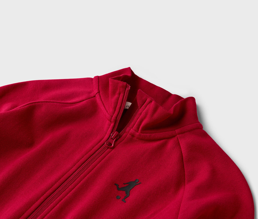 Gros plan sur un survêtement rouge avec fermeture éclair et petit logo de joueur de football.