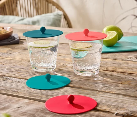 Deux verres de boissons sont posés sur une table en bois, chacun fermé par un couvercle en silicone, un turquoise et un rouge.