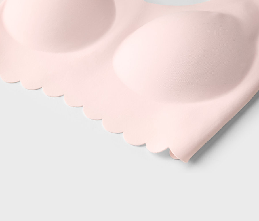 Gros plan d'un soutien-gorge rose clair avec un bord ondulé sur fond blanc.