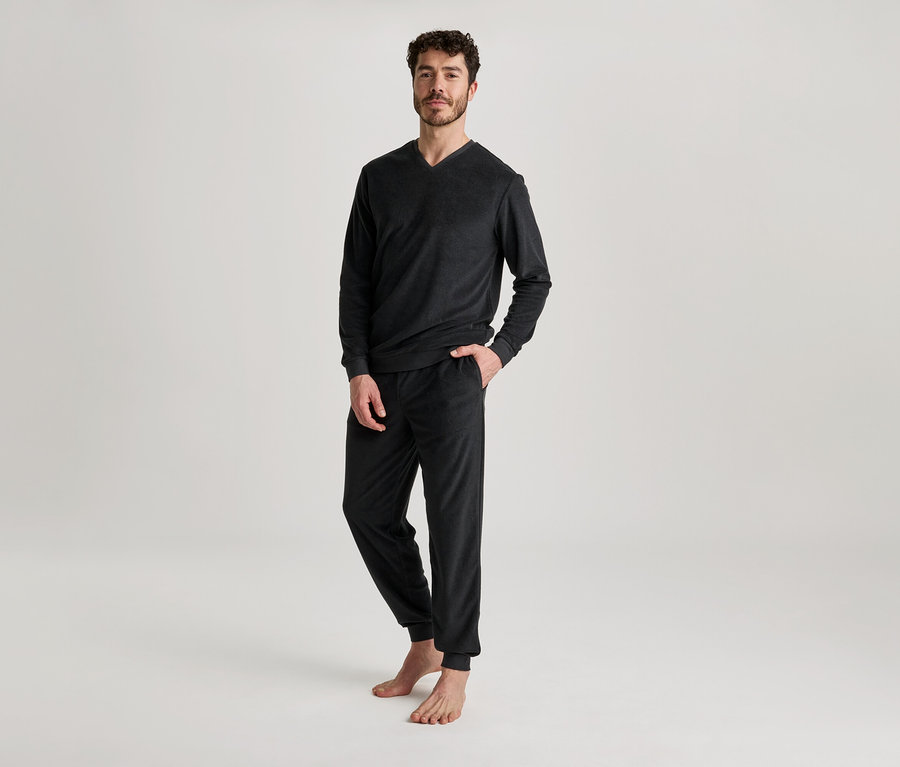 Homme portant un haut noir à manches longues et col en V et un pantalon de jogging, une main dans la poche.