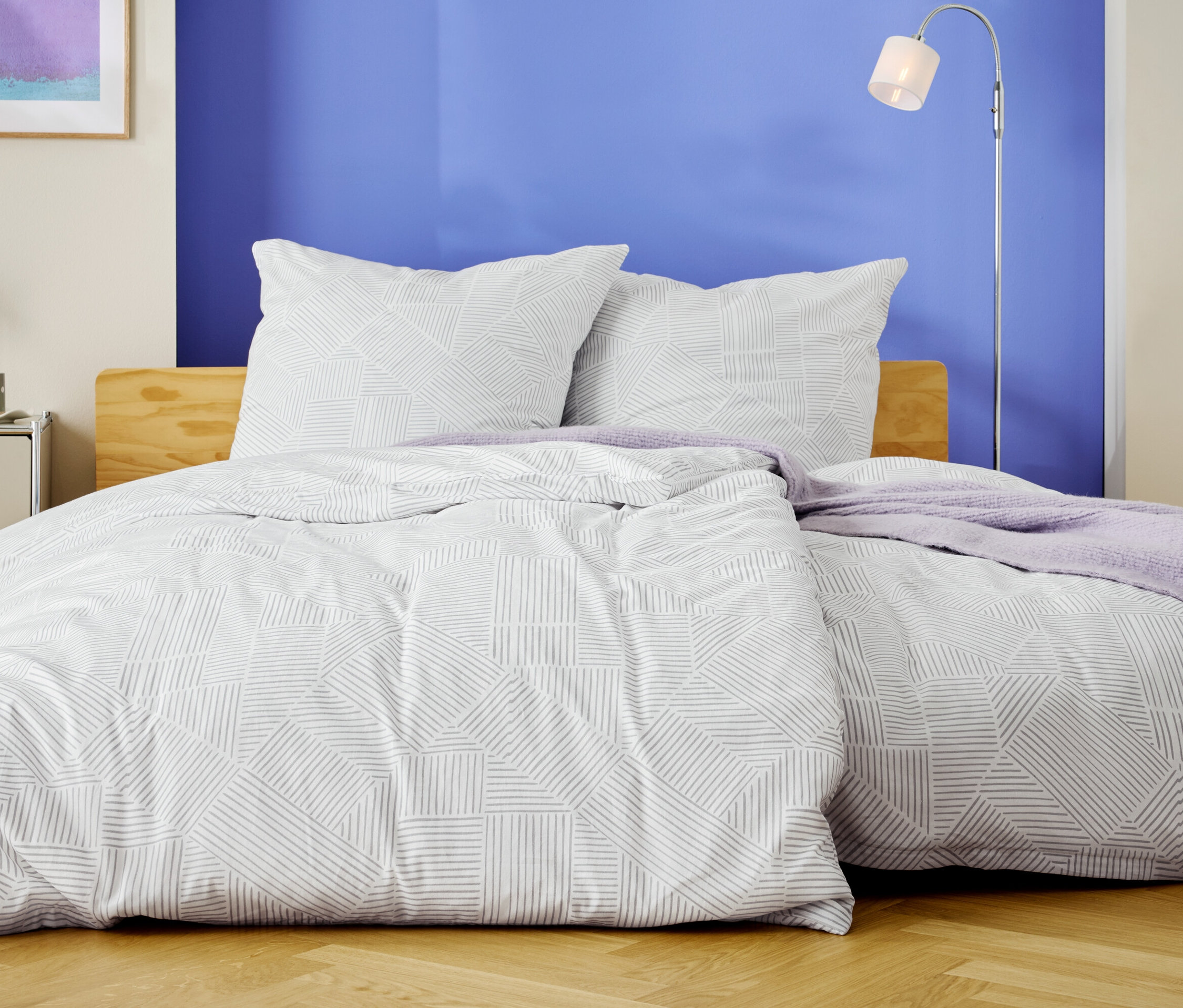 Un lit avec des draps blancs à motifs géométriques et deux oreillers se dresse devant un mur bleu.