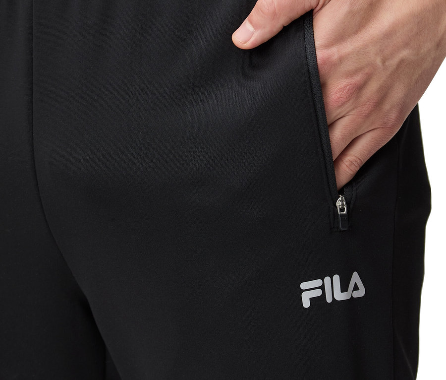 Un homme met sa main dans la poche d'un pantalon de survêtement FILA noir.