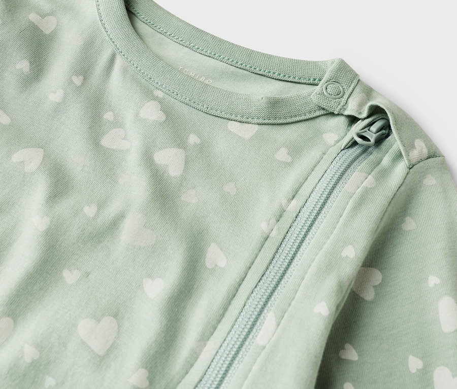 Gros plan d'une gigoteuse vert clair pour bébé avec un motif de cœurs blancs et une fermeture éclair.