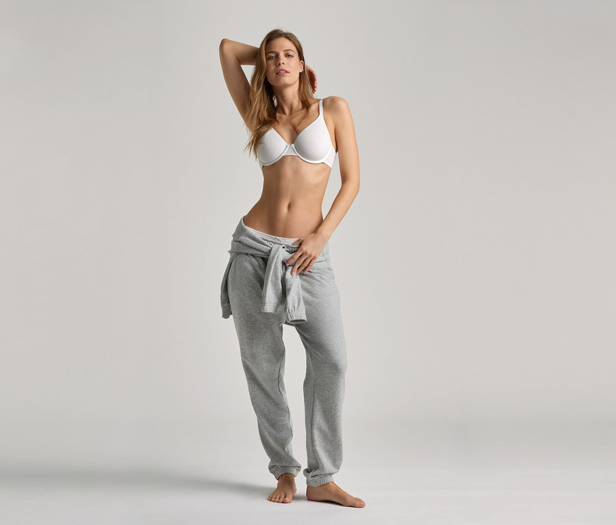 Femme posant en soutien-gorge blanc et pantalon de survêtement gris.