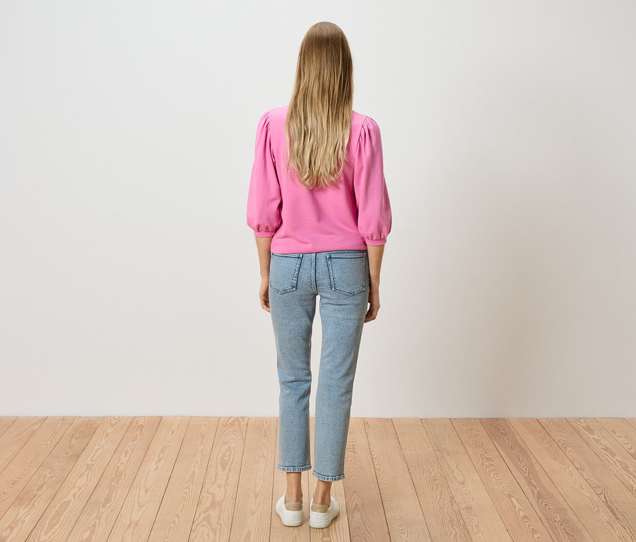 Vue arrière d'une femme aux cheveux blonds portant un pull rose et un jean bleu clair.