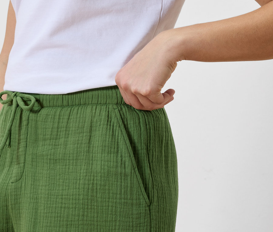 Une femme met la main dans la poche d'un pantalon vert à cordon, avec un t-shirt blanc.