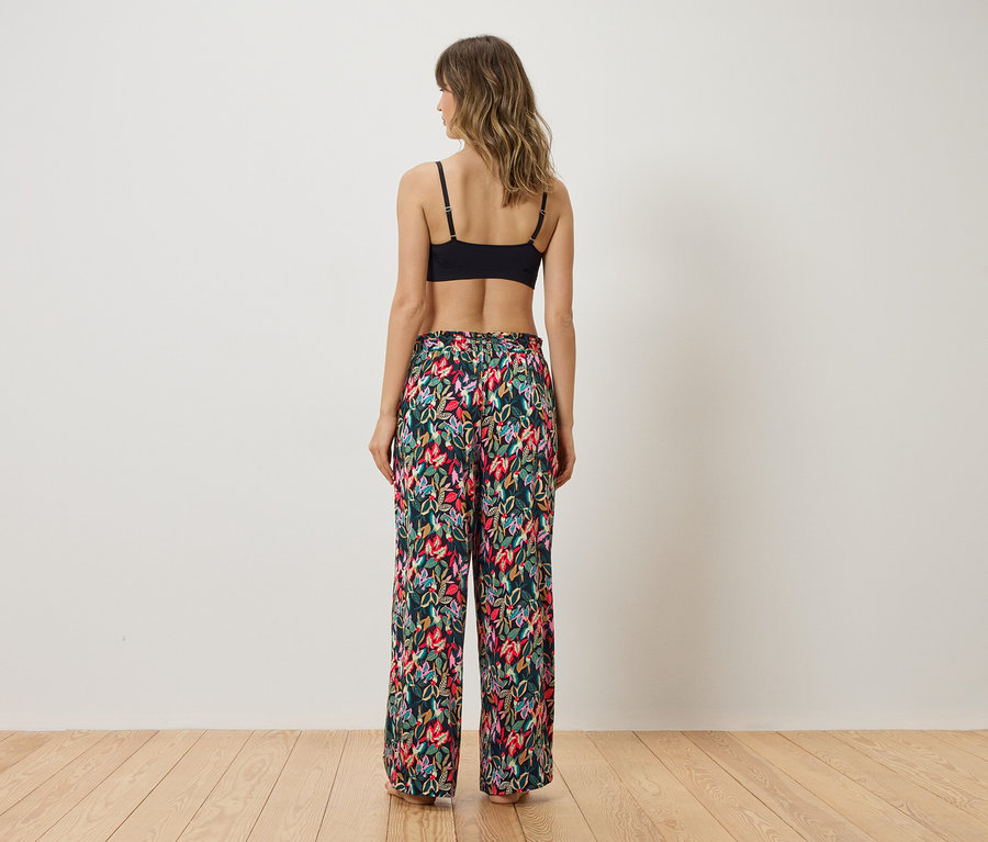 Femme vue de dos portant un soutien-gorge noir et un pantalon de pyjama à fleurs.