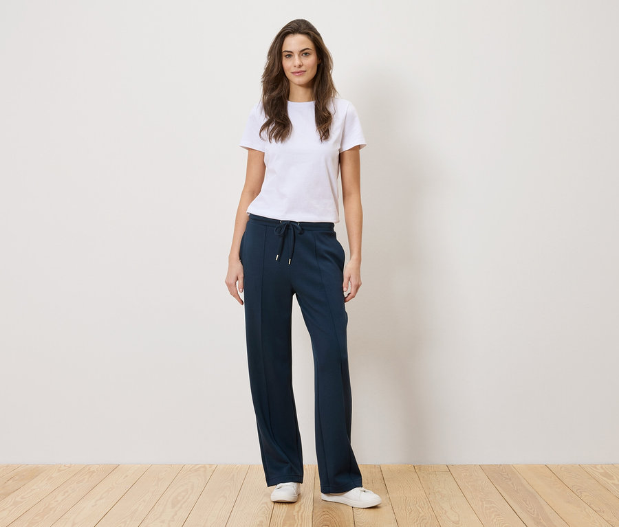 Femme debout portant un t-shirt blanc et un pantalon bleu marine.