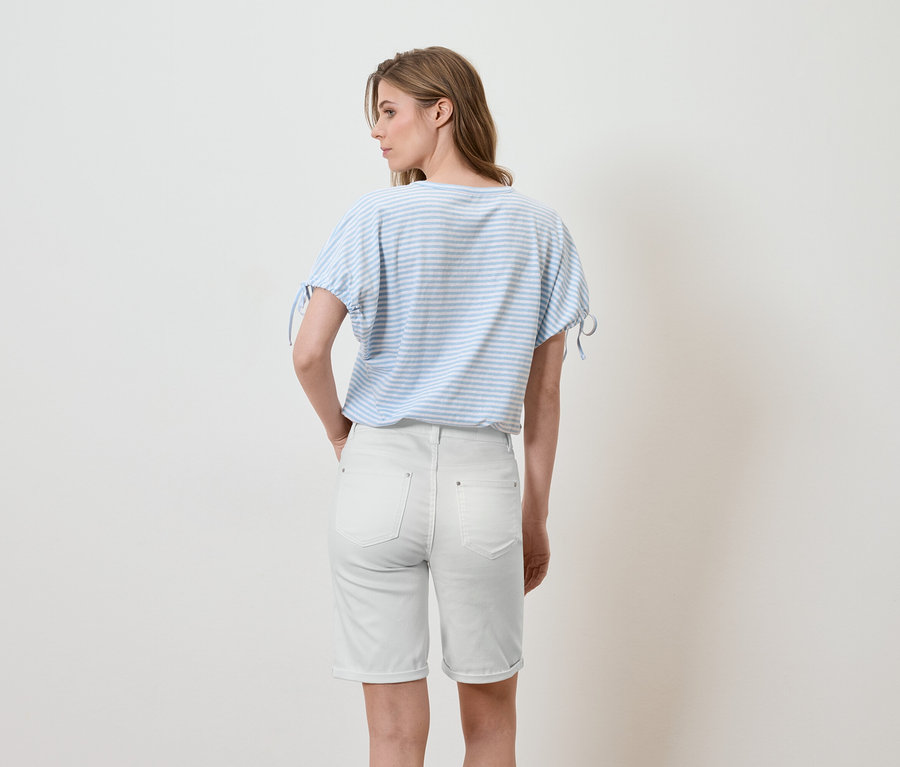 Une femme se tient dos à la caméra, portant un t-shirt à rayures bleues et blanches et un short en jean clair.